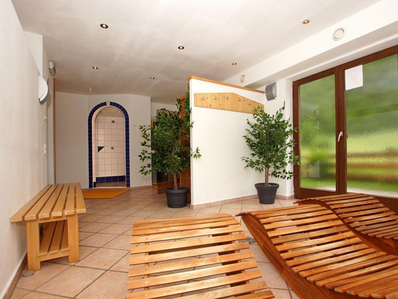 Spa relaxation room with wooden loungers, bench, potted plants, and glass door to outside.