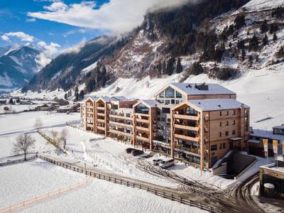 Duży hotel z drewnianą elewacją i balkonami w ośnieżonym górskim krajobrazie.