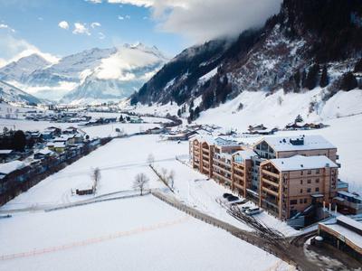 Zaśnieżony krajobraz górski z dużym budynkiem hotelowym i małą wioską w dolinie.