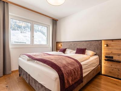 Jasna sypialnia z dużym łóżkiem podwójnym, drewnianą podłogą i oknem z zasłonami.