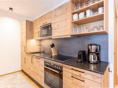 Nowoczesny aneks kuchenny z drewnianymi frontami, czarnymi blatami i sprzętem w pokoju hotelowym.