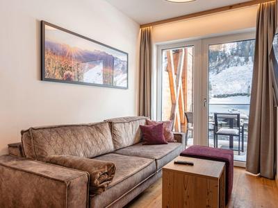 Nowoczesny salon z brązową sofą, małym drewnianym stolikiem i dostępem do balkonu.