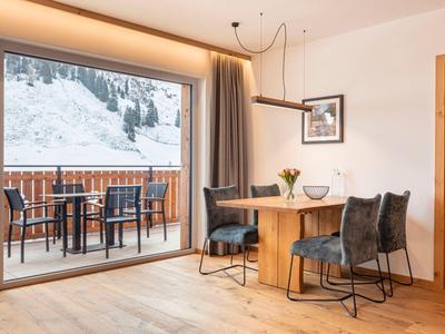 Przytulny jadalnia z drewnianym stołem i krzesłami, duży balkon z widokiem na góry w tle.