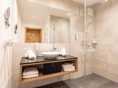 Nowoczesna łazienka z podwójną umywalką, dużym lustrem i prysznicem bez brodzika.