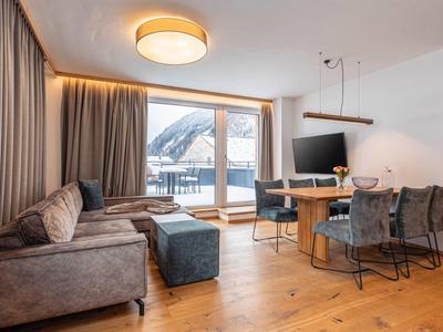 Nowoczesny salon z brązową sofą, telewizorem, stołem jadalnym i widokiem na góry przez duże okna.