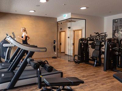 Moderner Fitnessraum mit Laufbändern, Trainingsgeräten und einer Frau, die auf dem Laufband trainiert.