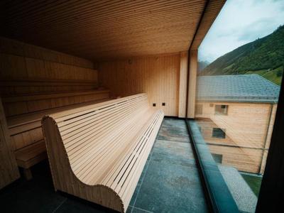 Nowoczesna sauna z zakrzywionymi drewnianymi ławkami i panoramicznym oknem z widokiem na góry.