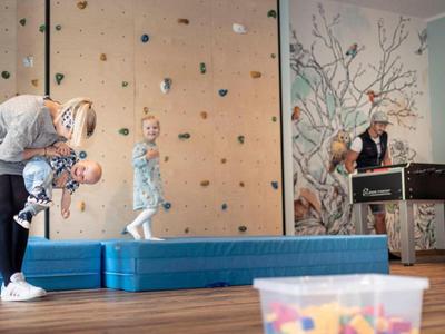 Dzieci bawiące się w pomieszczeniu z ścianką wspinaczkową i miękkimi matami w tle.