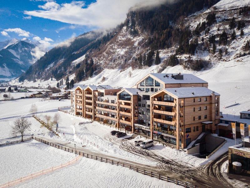 Duży hotel z drewnianą elewacją i balkonami w ośnieżonym górskim krajobrazie.