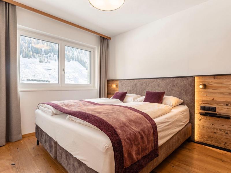 Jasna sypialnia z dużym łóżkiem podwójnym, drewnianą podłogą i oknem z zasłonami.