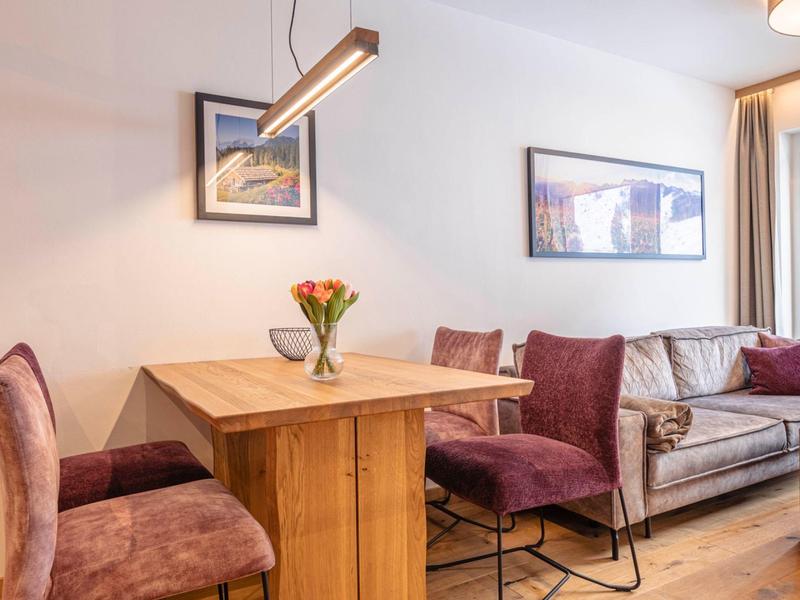 Przytulna jadalnia z drewnianym stołem, bukietem kwiatów i fioletowymi tapicerowanymi krzesłami obok sofy.