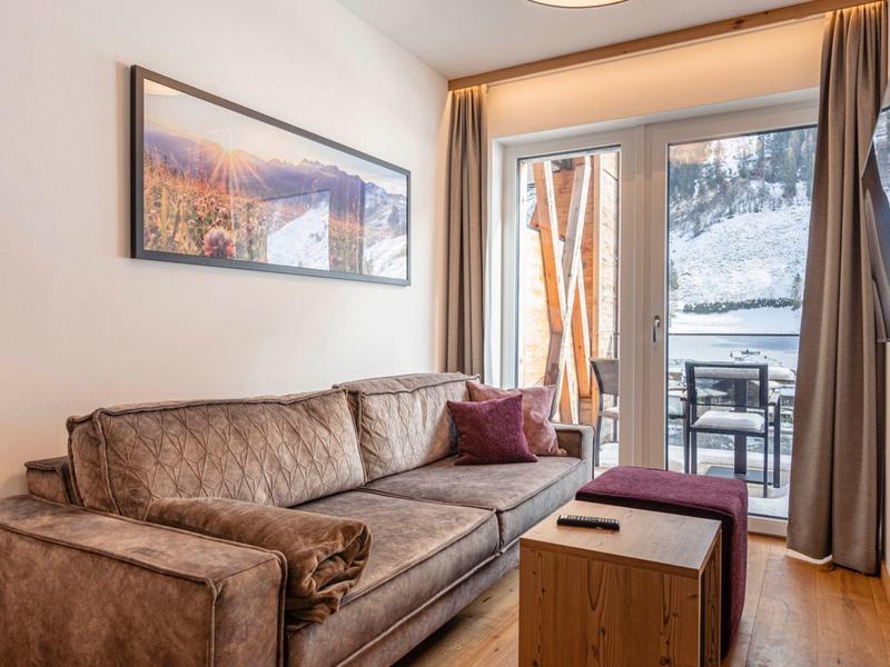 Nowoczesny salon z brązową sofą, małym drewnianym stolikiem i dostępem do balkonu.