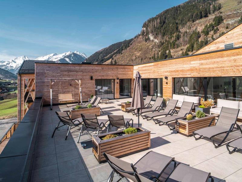 Taras z leżakami i miejscami do siedzenia na tle gór i niebieskiego nieba.