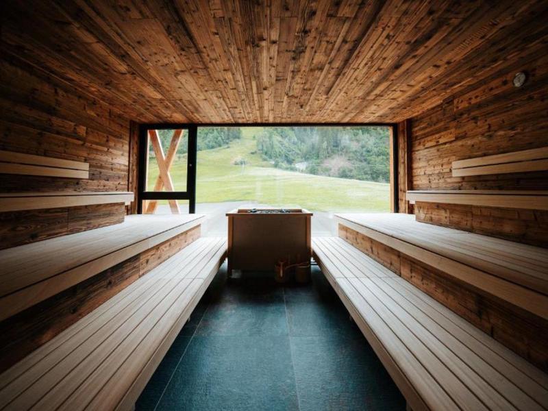 Pokój sauny z drewnianymi ścianami i ławkami, duże okno z widokiem na zielony krajobraz