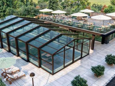 Střešní terasa se skleněným krytem a posezením s slunečníky obklopená zelení.