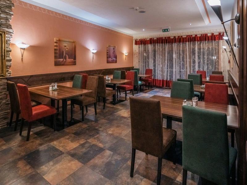 Gemütlicher Speiseraum mit bunten Stühlen, Holztischen und warmem Licht.