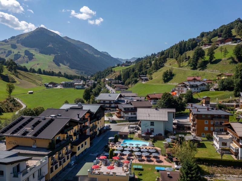 Blick auf ein Bergdorf mit Hotel, Pool und grünen Hügeln bei klarem Himmel.