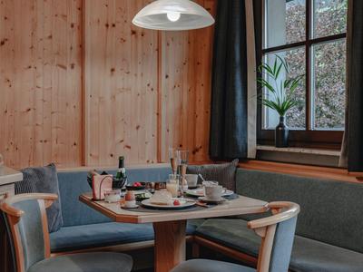 Gemütlicher Essbereich mit Holzwänden, gepolsterten Sitzbänken und Stühlen, Fenster mit Pflanze.