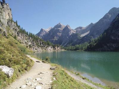 Turistická trasa podél horského jezera s čistou tyrkysovou vodou a skalnatými horami v pozadí