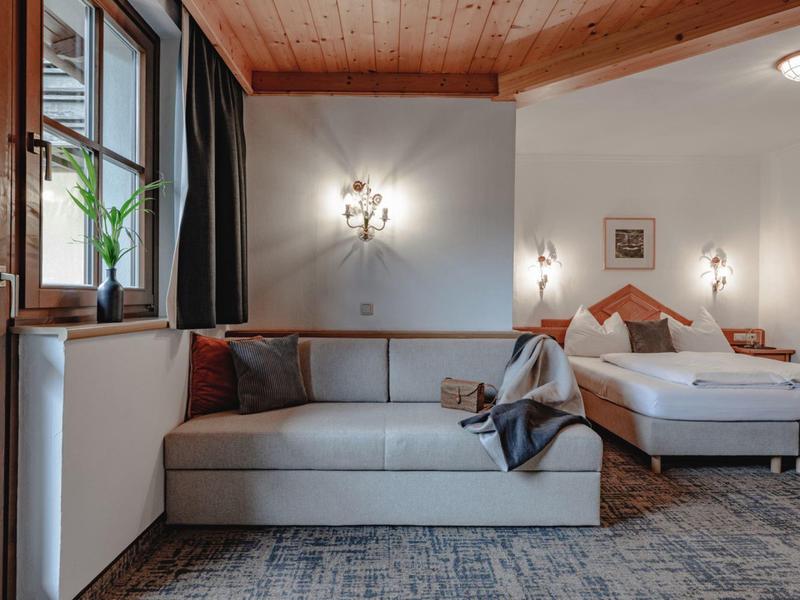 Pohodlný hotelový pokoj s pohovkou, postelí a teplými dřevěnými prvky.