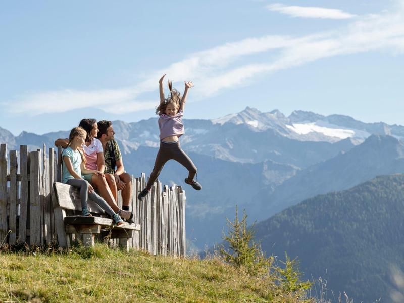 Skupina lidí na horách, jedna osoba skáče ze plotu na horském pozadí