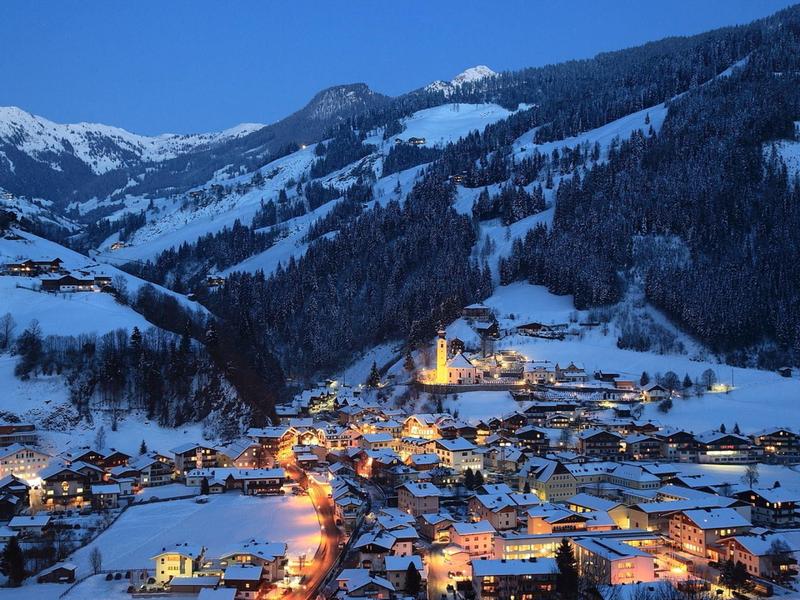 Zimní horská vesnice v noci s osvětlenými domy a zasněženými svahy.