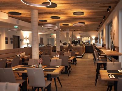 A modern restaurant with brown chairs and wooden tables, warmly lit with columns.