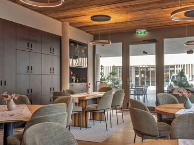 Area lounge accogliente dell'hotel con mobili in legno e grandi finestre che si affacciano all'esterno.