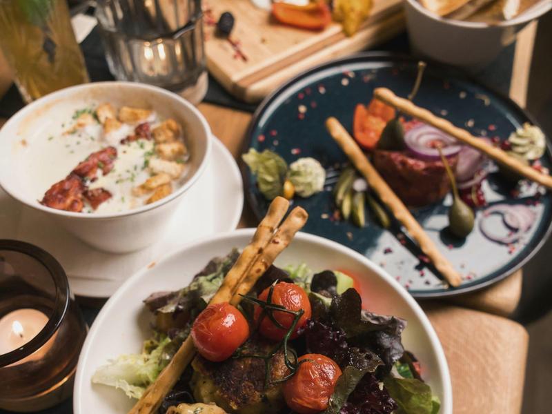 Eine bunte Mahlzeit mit Salat, Cherry-Tomaten, Gemüse und einer Suppe in weißen Schüsseln.