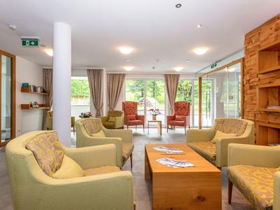 Salon lumineux avec fauteuils confortables, table en bois et grandes fenêtres donnant sur la verdure.