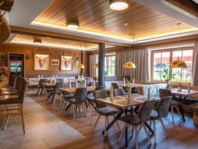 Salle de restaurant d'hôtel moderne avec sols en bois et tables dressées à la lumière du jour.