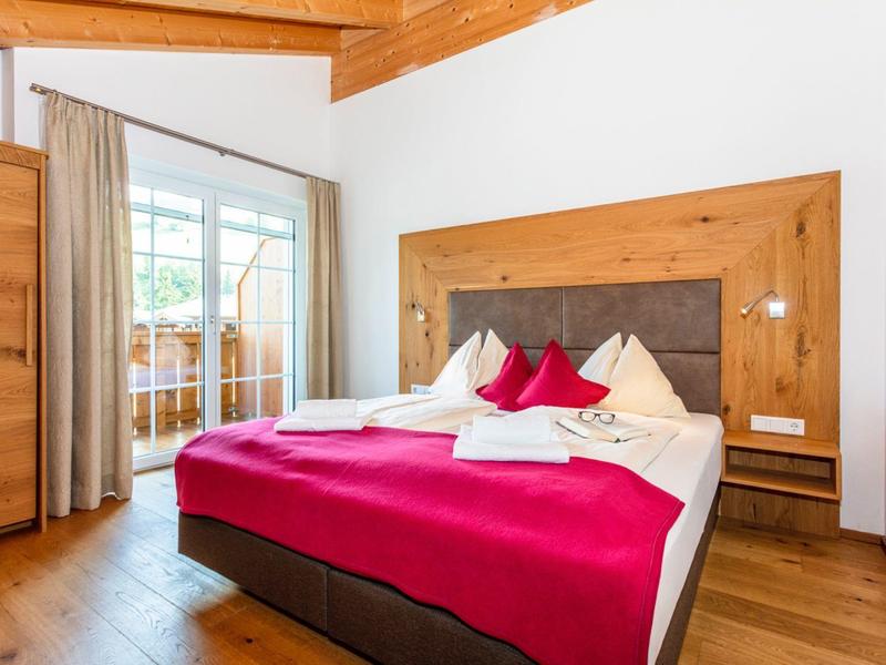 Světý hotelový pokoj s velkou manželskou postelí, červenými přikrývkami a dřevěnými prvky.