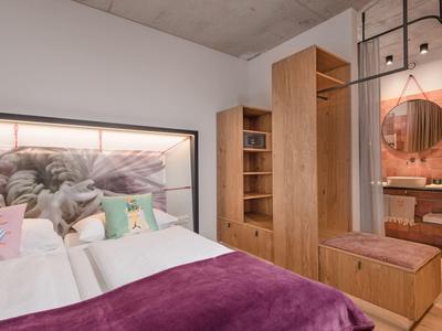 Camera d'hotel moderna con letto matrimoniale, coperta viola e mobili in legno