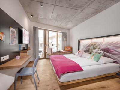 Camera d'hotel moderna con letto grande, scrivania, poltrona e balcone con porte in vetro.