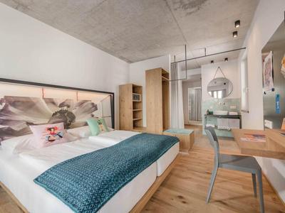Camera d'hotel arredata modernamente con letto matrimoniale, pavimento in legno e area lavoro