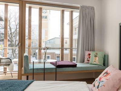 Camera luminosa con grande finestra, panca accogliente e cuscini con motivo floreale.