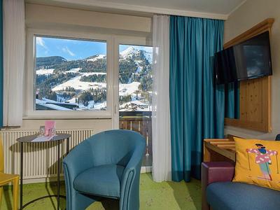 Camera d'hotel con poltrone, tavolo, TV e finestra con vista sulle montagne.