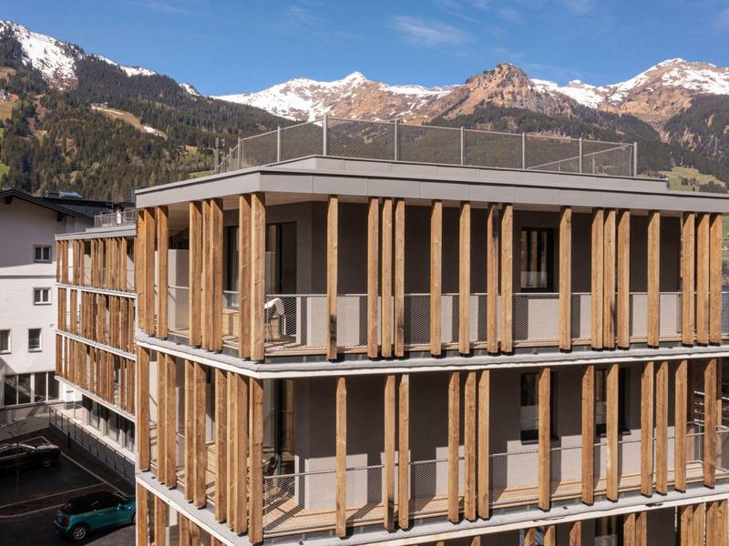 Edificio moderno in legno di due piani davanti a montagne innevate sotto un cielo azzurro.