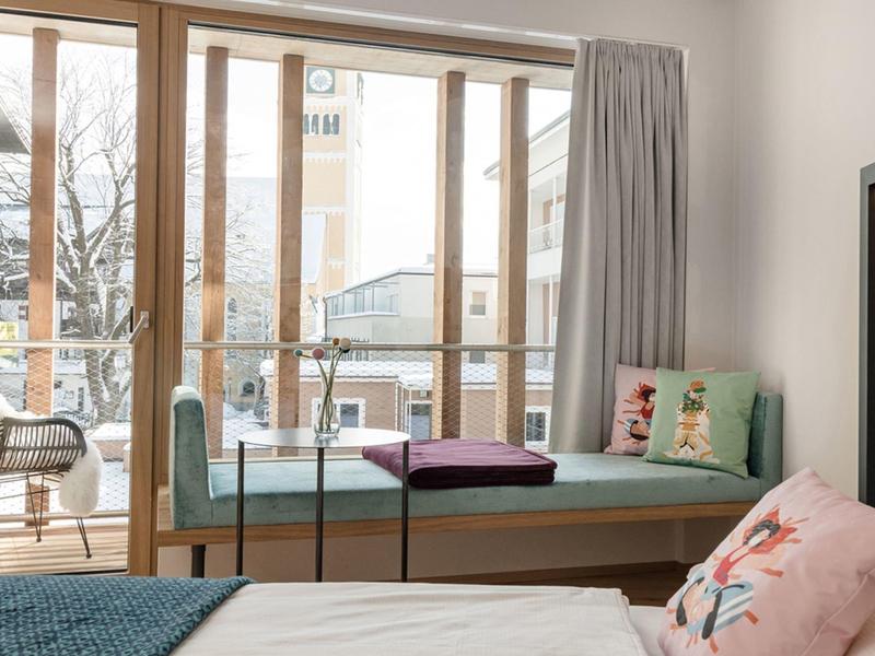 Camera luminosa con grande finestra, panca accogliente e cuscini con motivo floreale.