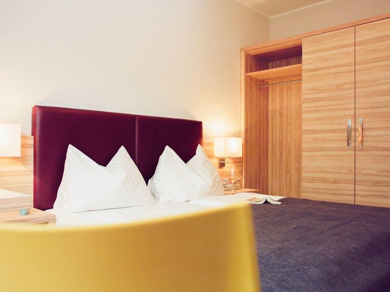 Camera d'hotel accogliente con letto matrimoniale, testiera rossa scura e mobili in legno.