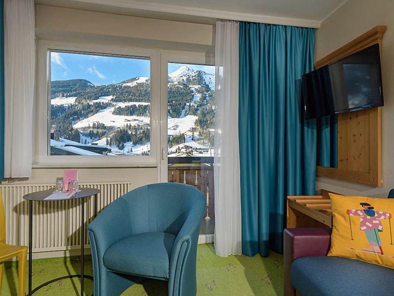 Camera d'hotel con poltrone, tavolo, TV e finestra con vista sulle montagne.