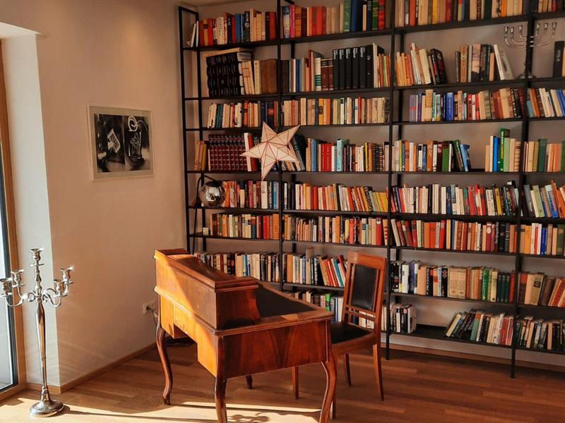 Accogliente sala lettura con scrivania in legno, sedia e scaffali pieni di libri sotto una luce calda.