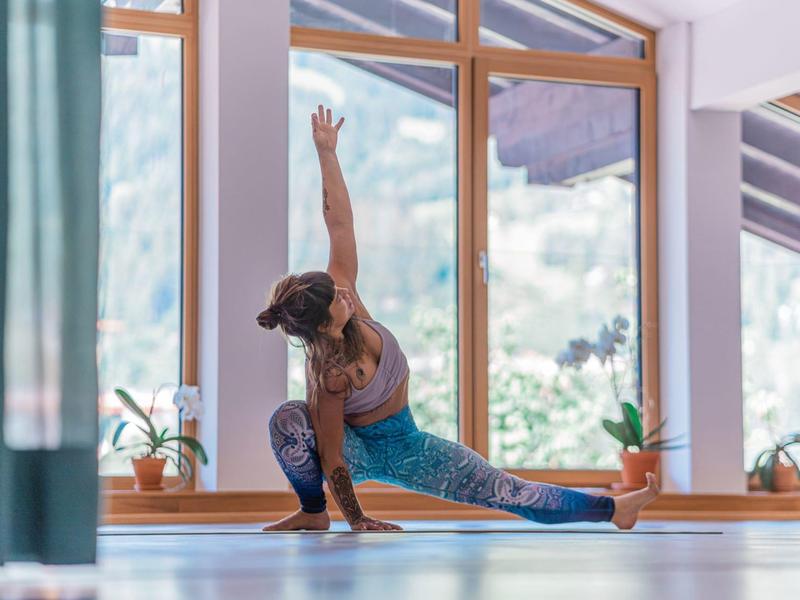 Donna che si allunga in una stanza luminosa vicino a grandi finestre con vista sulle montagne.