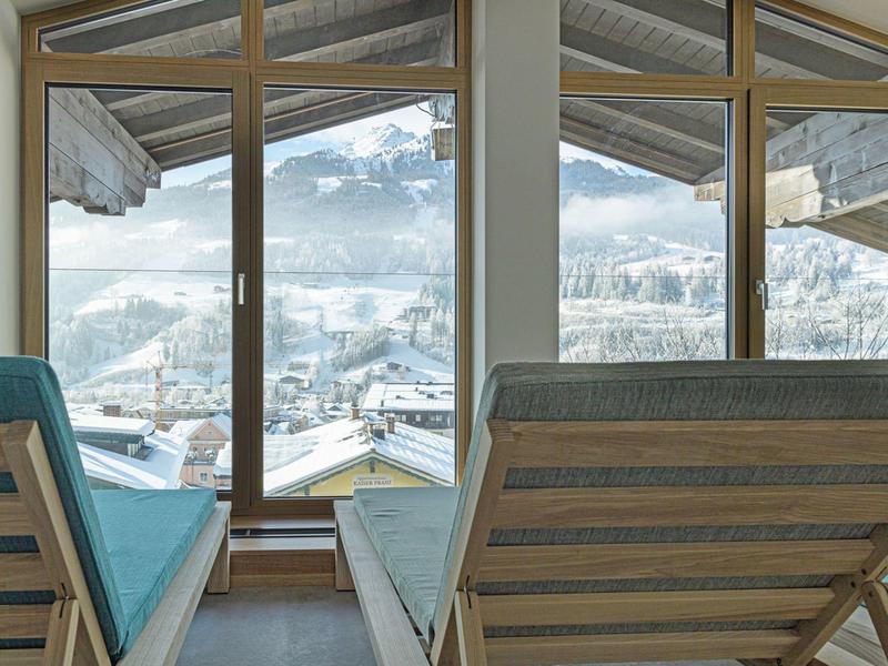 Due sdraio con cuscini blu davanti a grandi finestre con vista su montagne innevate.