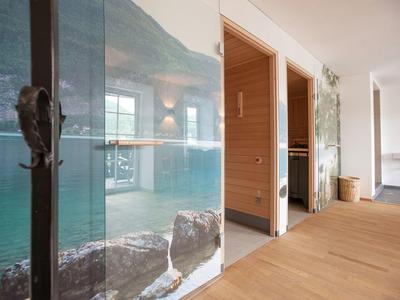 Nowoczesna strefa wellness z sauną, szklaną ścianą i drewnianą podłogą w jasnym pomieszczeniu.