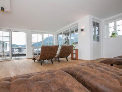 Jasny salon z dużymi oknami, widokiem na góry i skórzanymi fotelami na drewnianej podłodze.