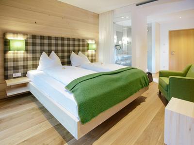 Modern eingerichtetes Hotelzimmer mit Doppelbett, grünem Bettüberwurf und gemütlichem Sessel.