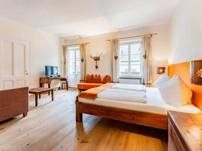 Helles Hotelzimmer mit Doppelbett, Sofa, Holzmöbeln und zwei Fenstern mit Vorhängen.