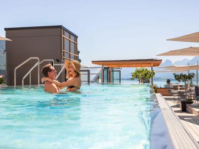 Zwei Frauen entspannen in einem Dachpool mit Blick auf das Meer und Berge.
