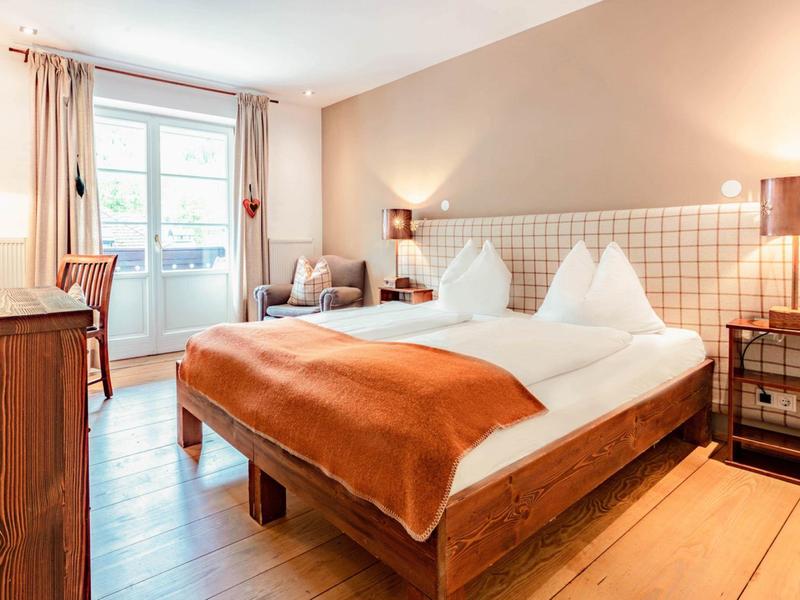 Przytulny pokój hotelowy z łóżkiem podwójnym, ciepłymi beżowymi tonami i balkonem z widokiem na zewnątrz.